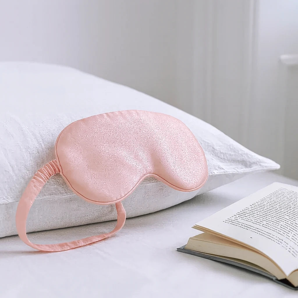 Masque de nuit en soie rose poudré posé sur l'oreiller